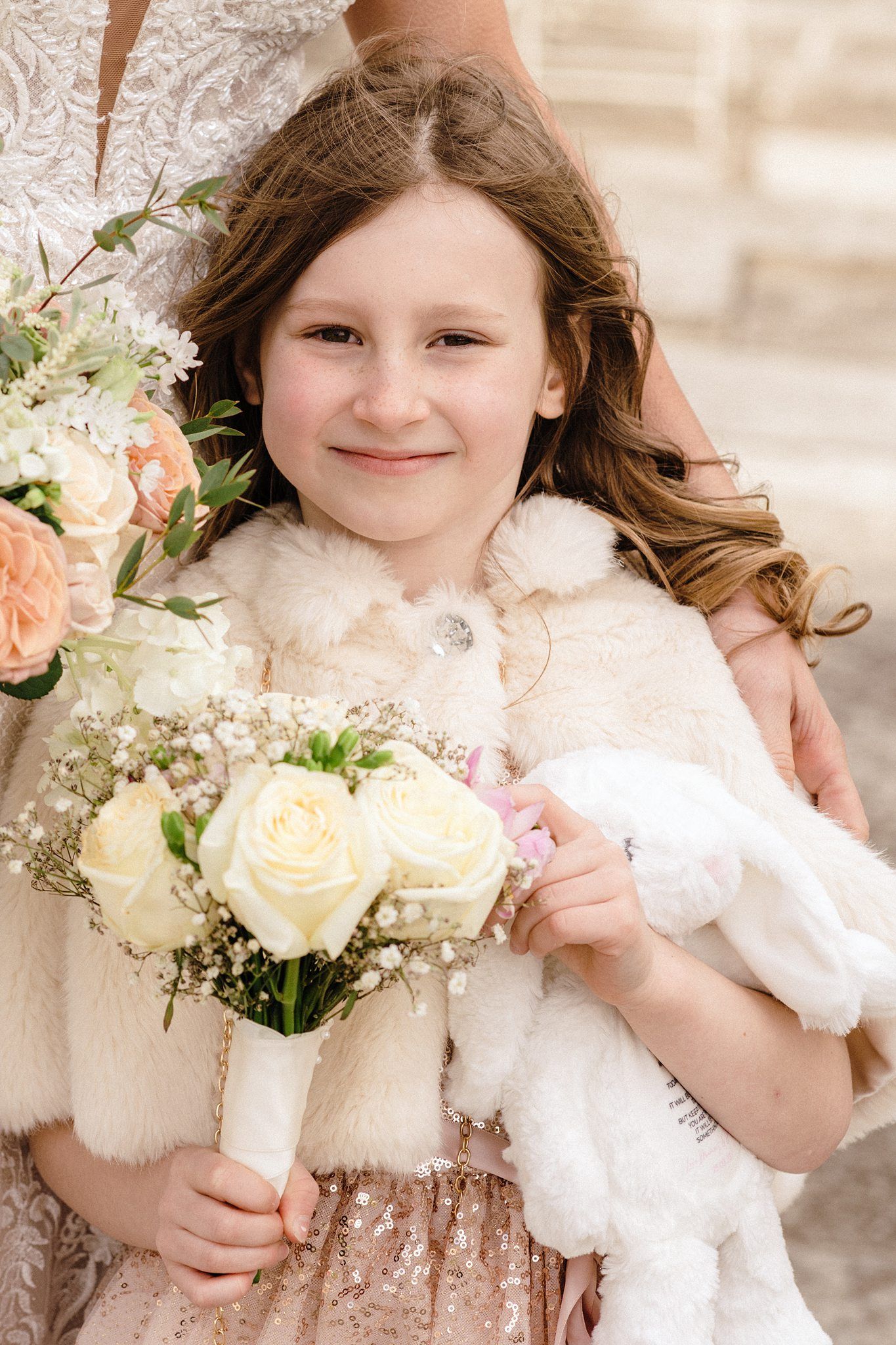 Nova Scotia wedding photographer captures young child in a white dress holding a bouquet of white roses with delicate baby's breath flowers.