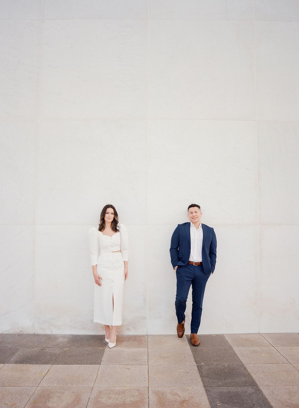 Minimalist photo series showing two people in white and navy outfits walking across a light gray wall background.