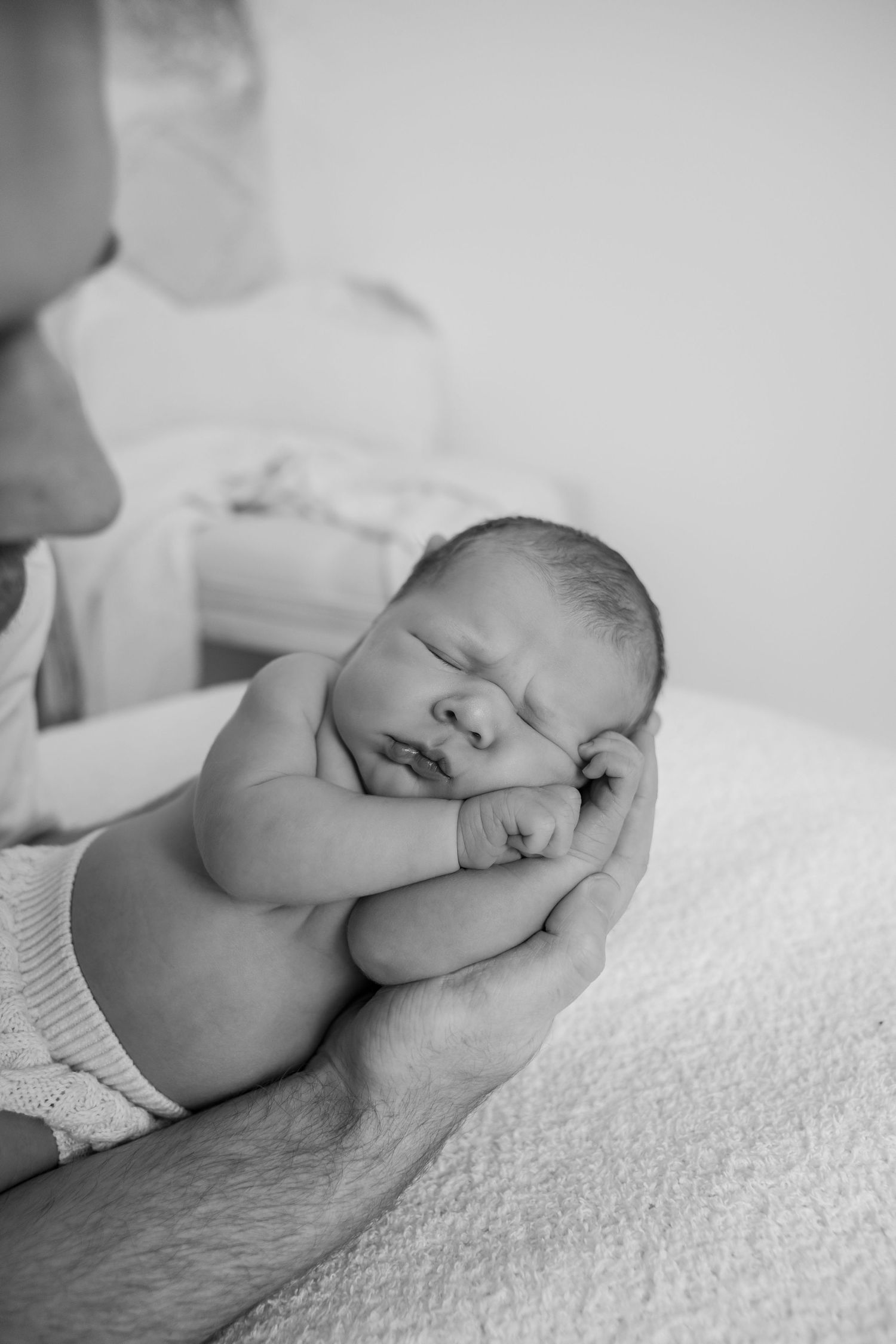 A series of black and white photos showing a sleeping newborn baby curled up on white fabric.