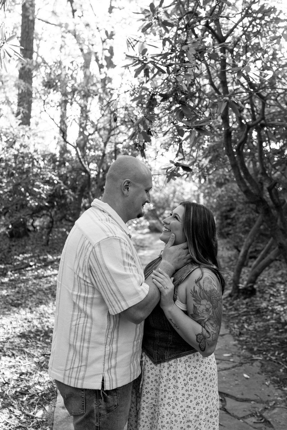 Black and white portrait of a smiling couple holding hands and gazing at each other outdoors.