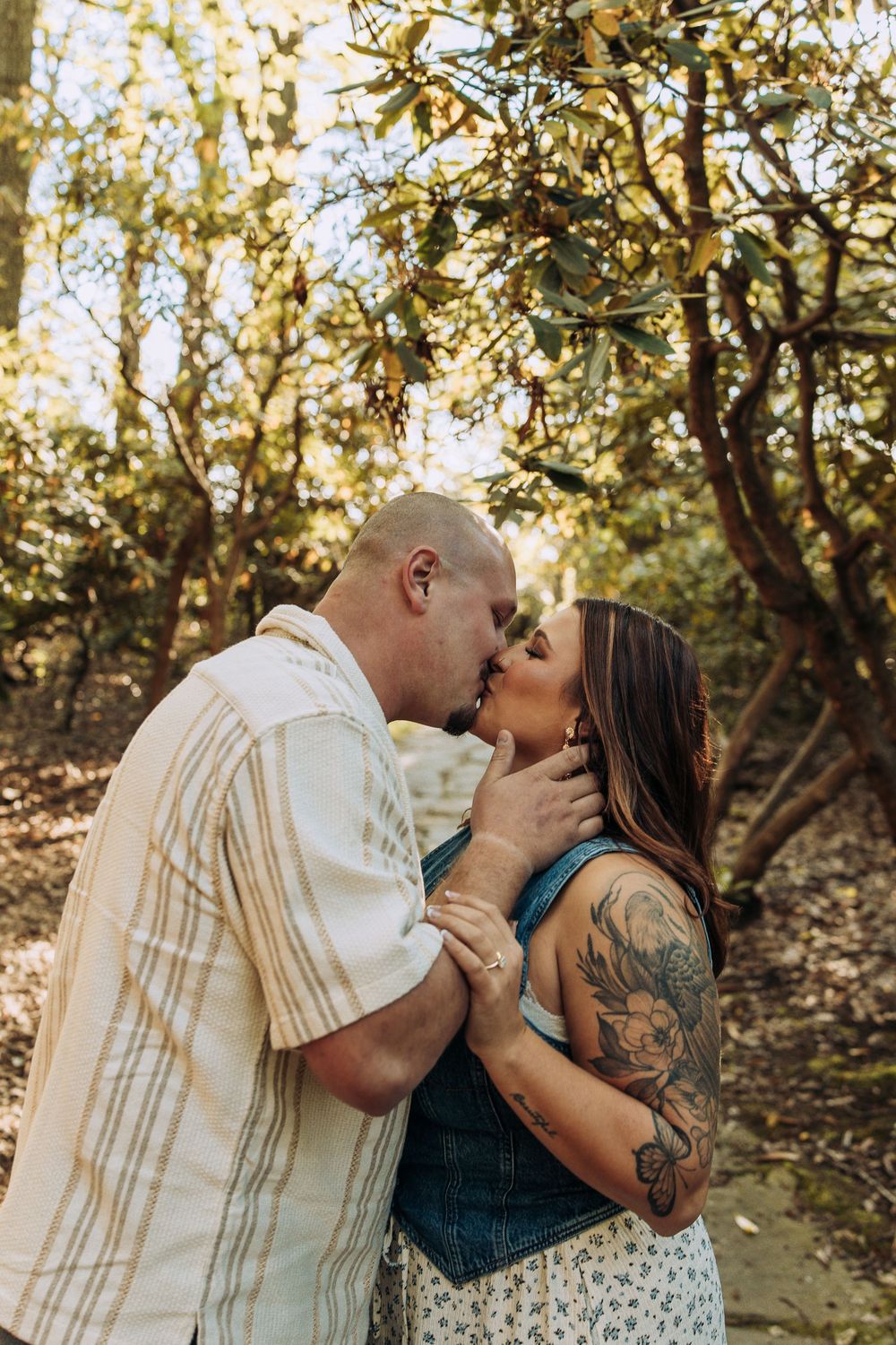 Couple sharing a kiss under sunlit tree branches on a stone garden path.