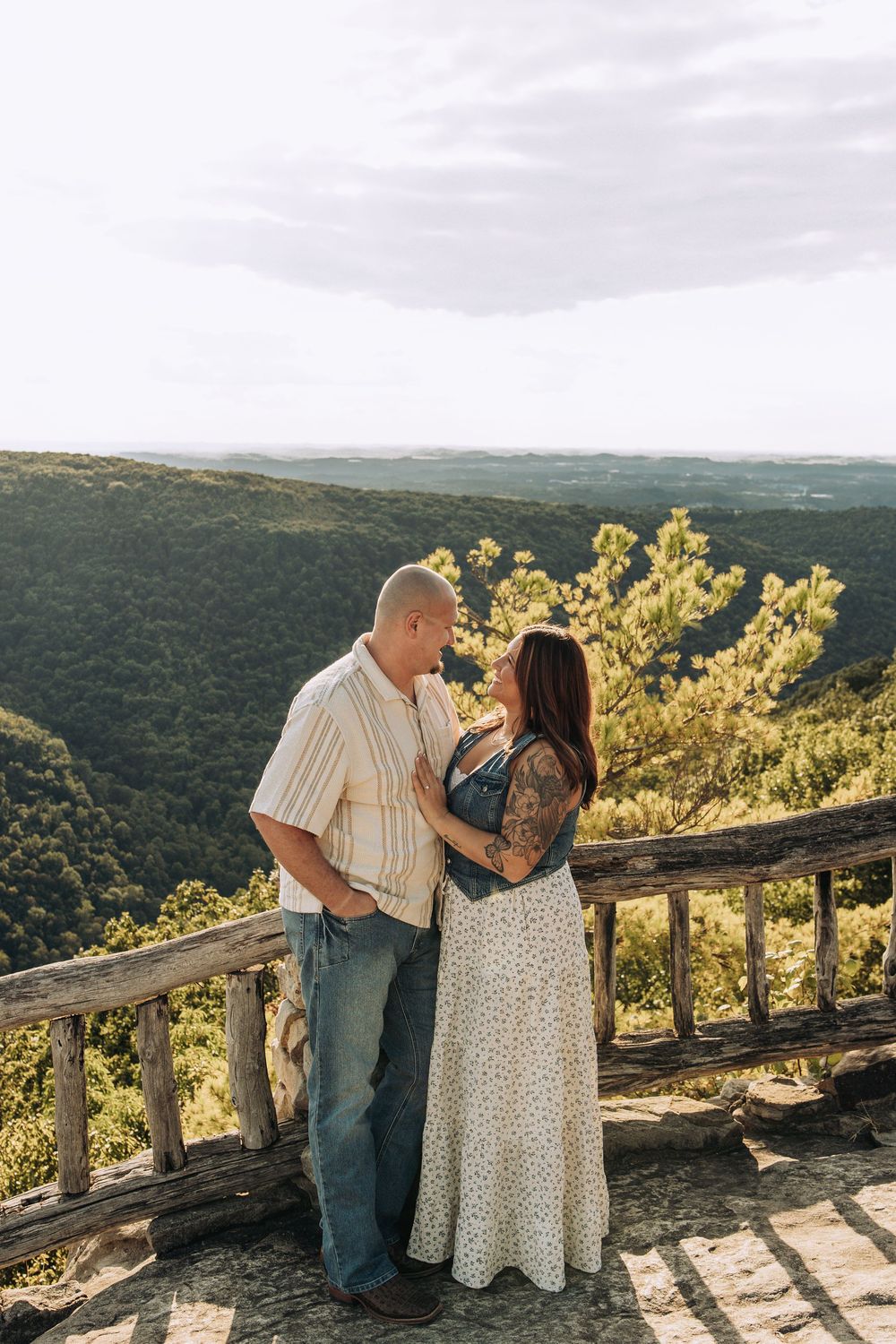 Couple standing close together at a rustic wooden overlook with a sweeping mountain valley view.