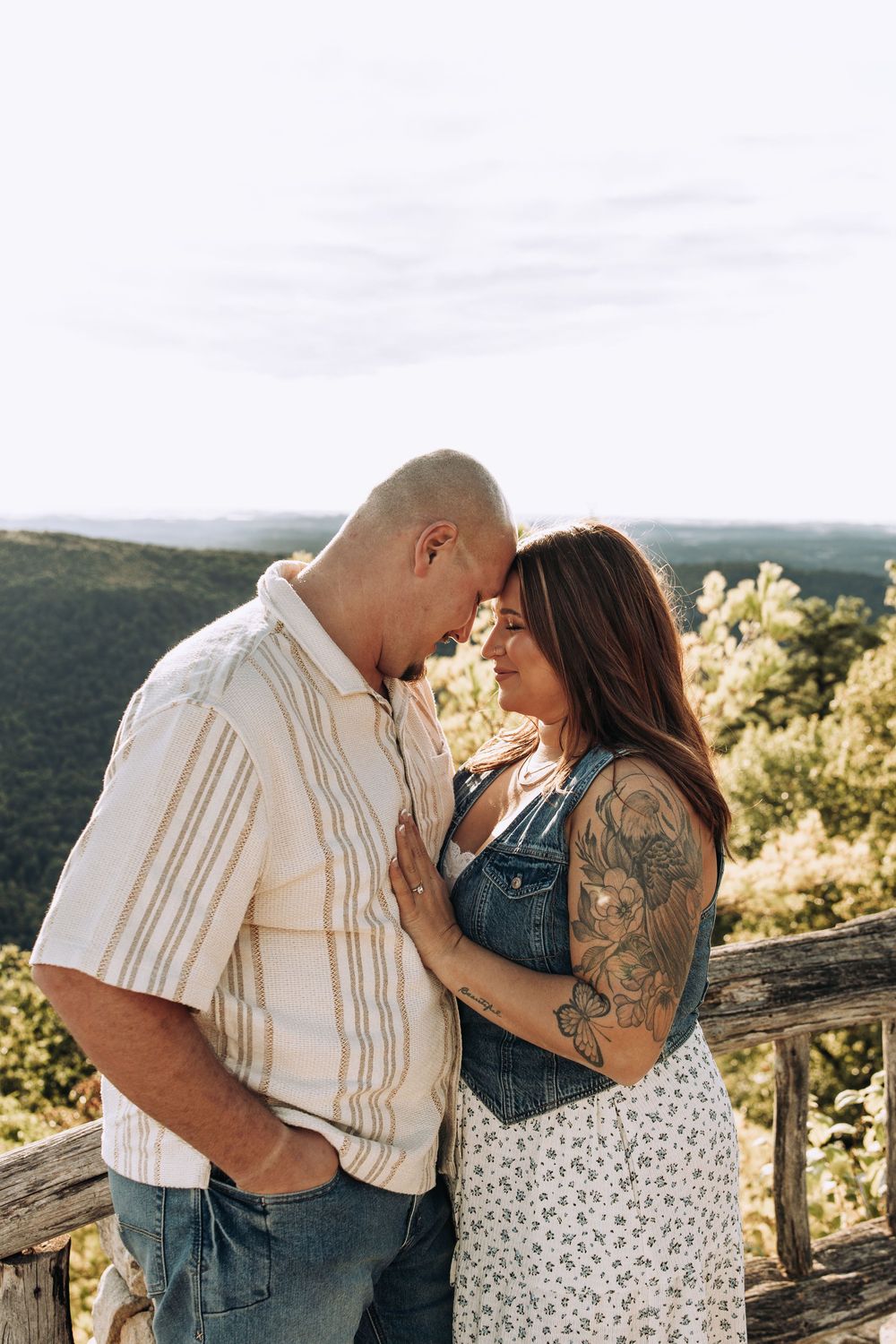 Couple touching foreheads intimately at a mountain overlook with rolling green hills behind them.