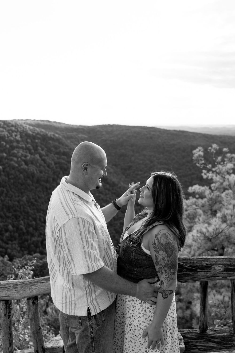 Black and white photo of a couple smiling at each other at a mountain overlook railing.