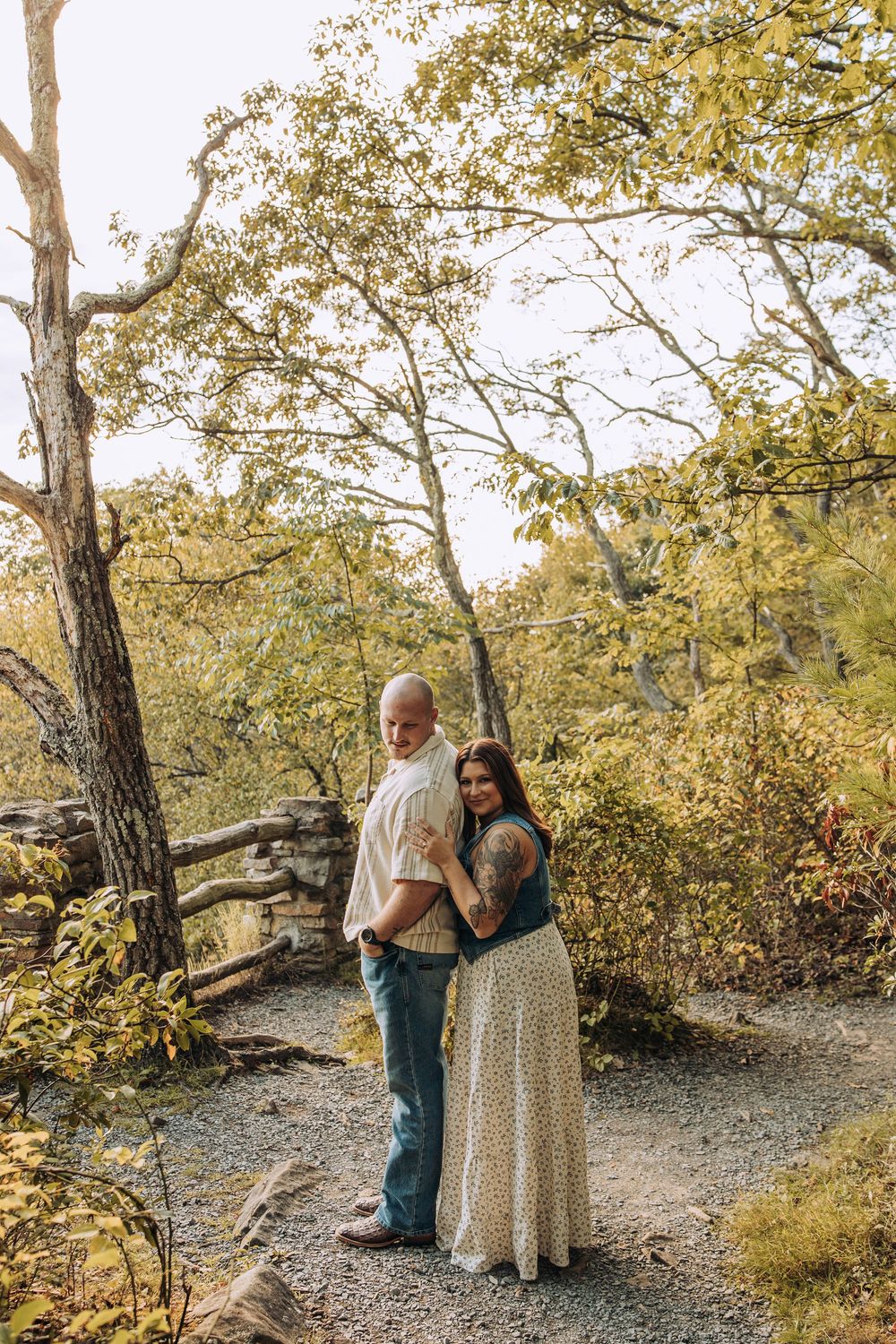 Engaged couple posing together on a forest trail surrounded by golden autumn foliage.