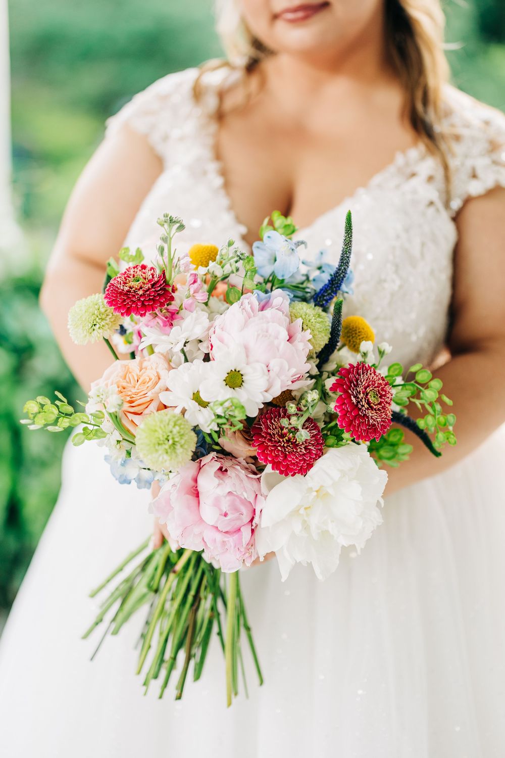 A vibrant bridal bouquet with pink peonies, red dahlias, white hydrangeas and wildflowers against a lace wedding dress at The Wild Flower 30