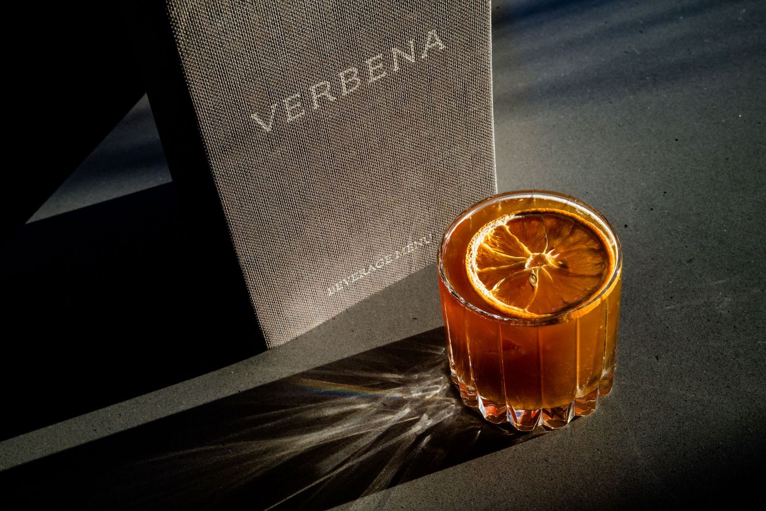 Dried orange slices and tea leaves arranged artistically with soft lighting and Verbena text in background.
