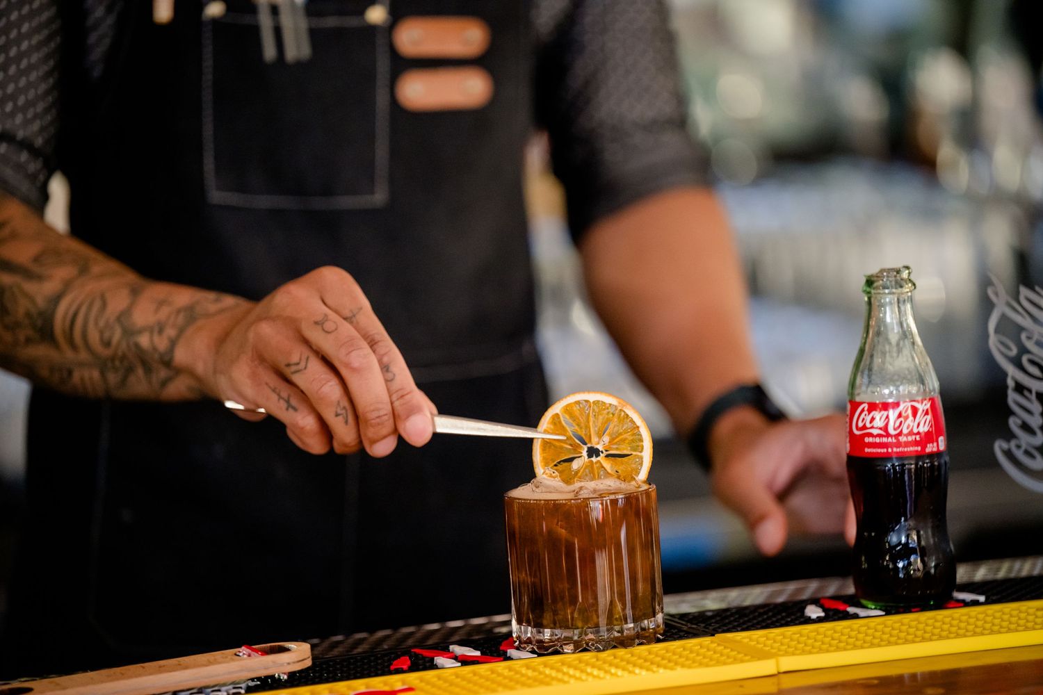 A bartender garnishes a cocktail with an orange slice at a dimly lit bar counter.