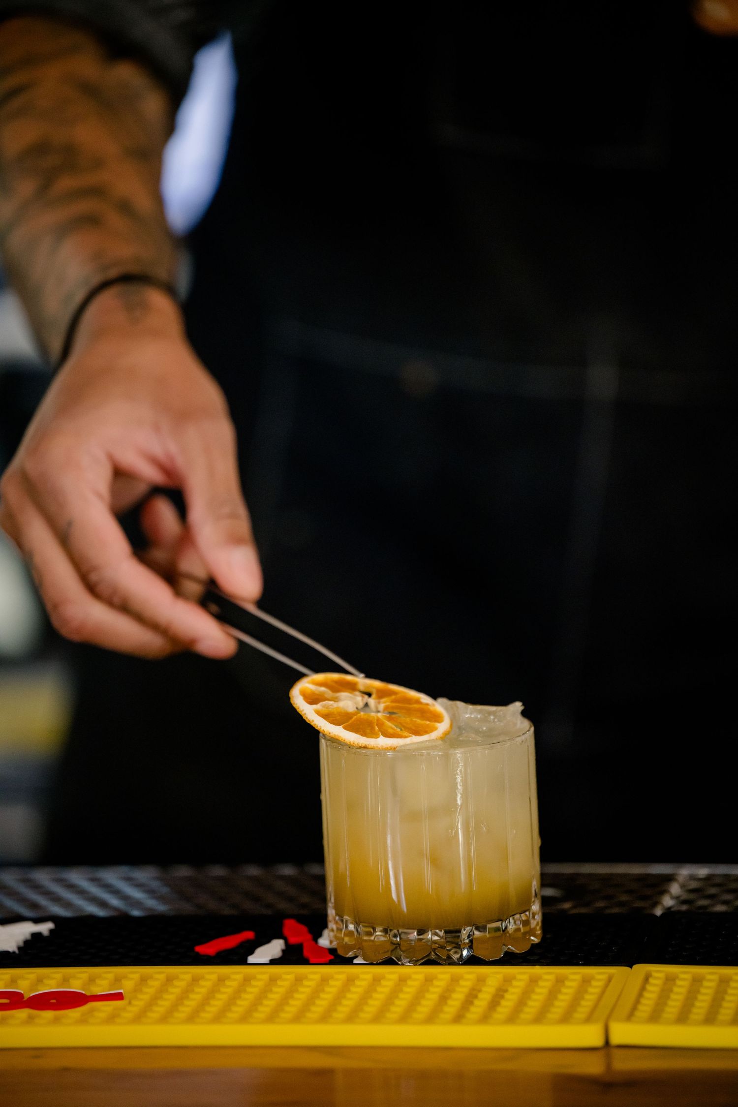A series of cocktail preparation shots showing hands garnishing a whiskey sour with an orange slice.