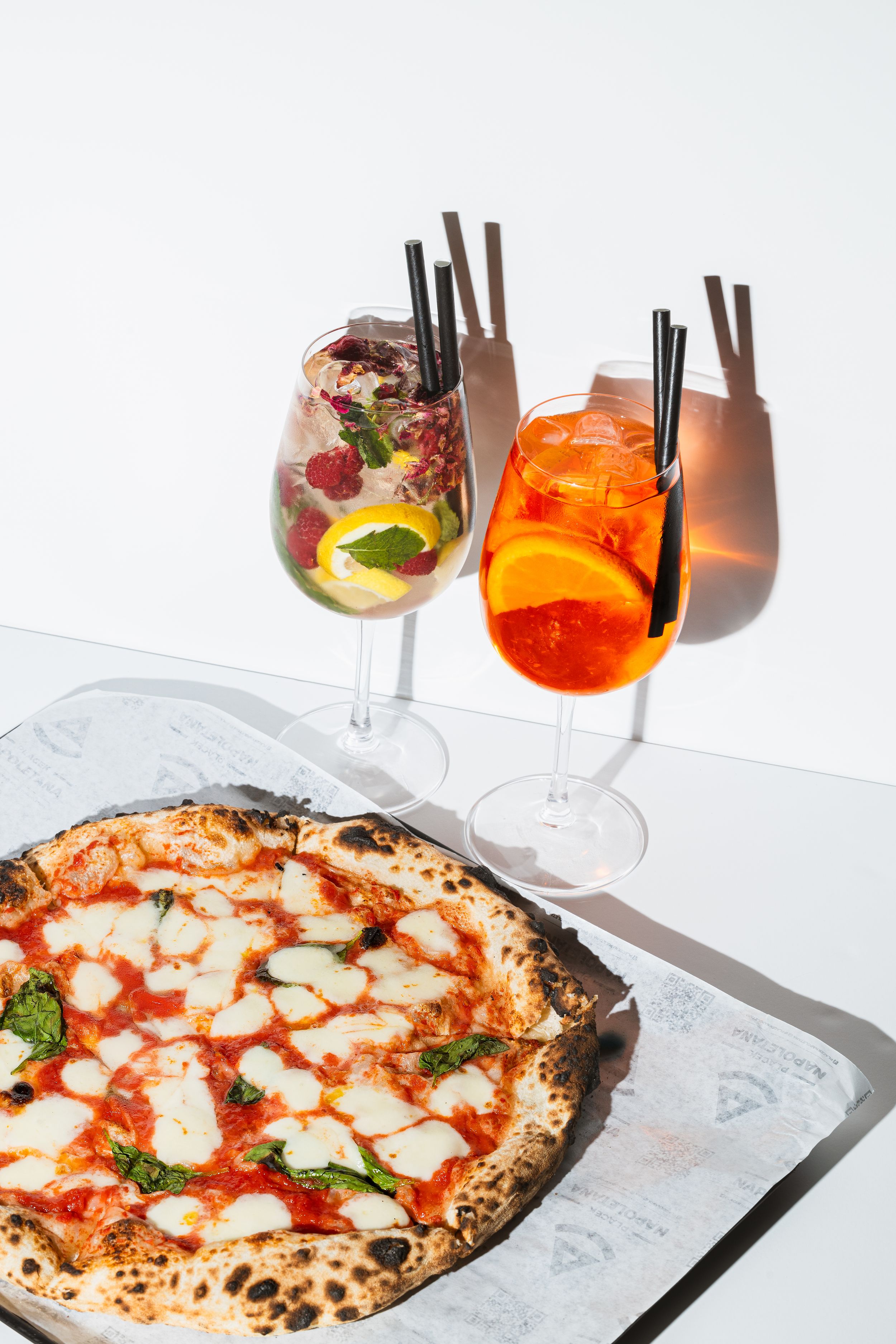 Pizza neapolitańska podana obok kolorowych koktajli na białym tle. Fotografia biznesowa Lublin.