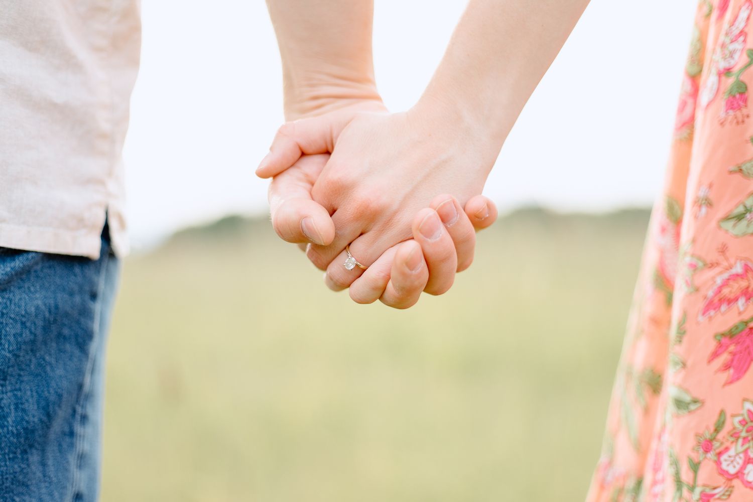 Close up view of hands holding a white rose against a soft blurred outdoor background.
