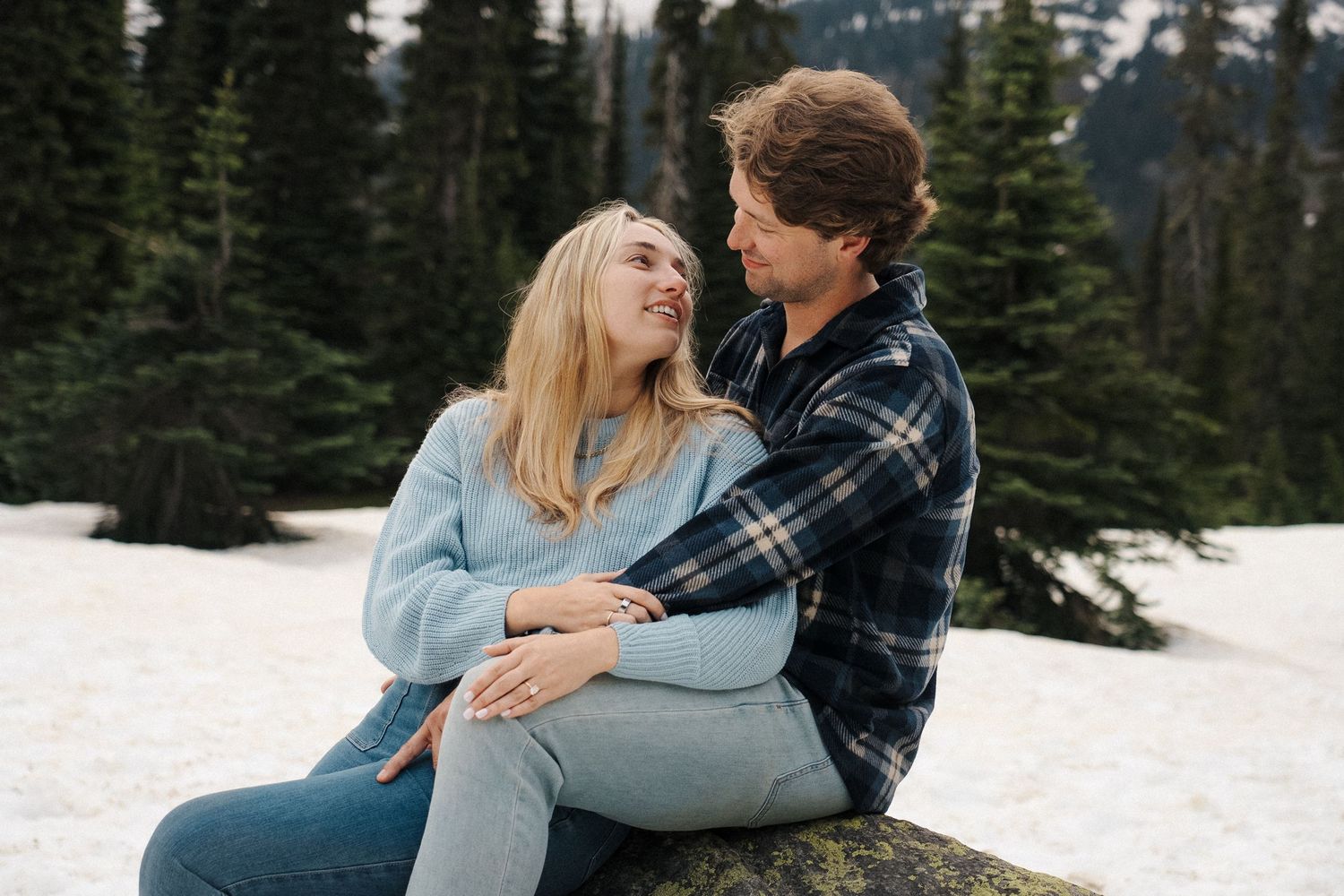 Couple enjoys intimate moments together during winter engagement photoshoot in snowy mountain forest setting.