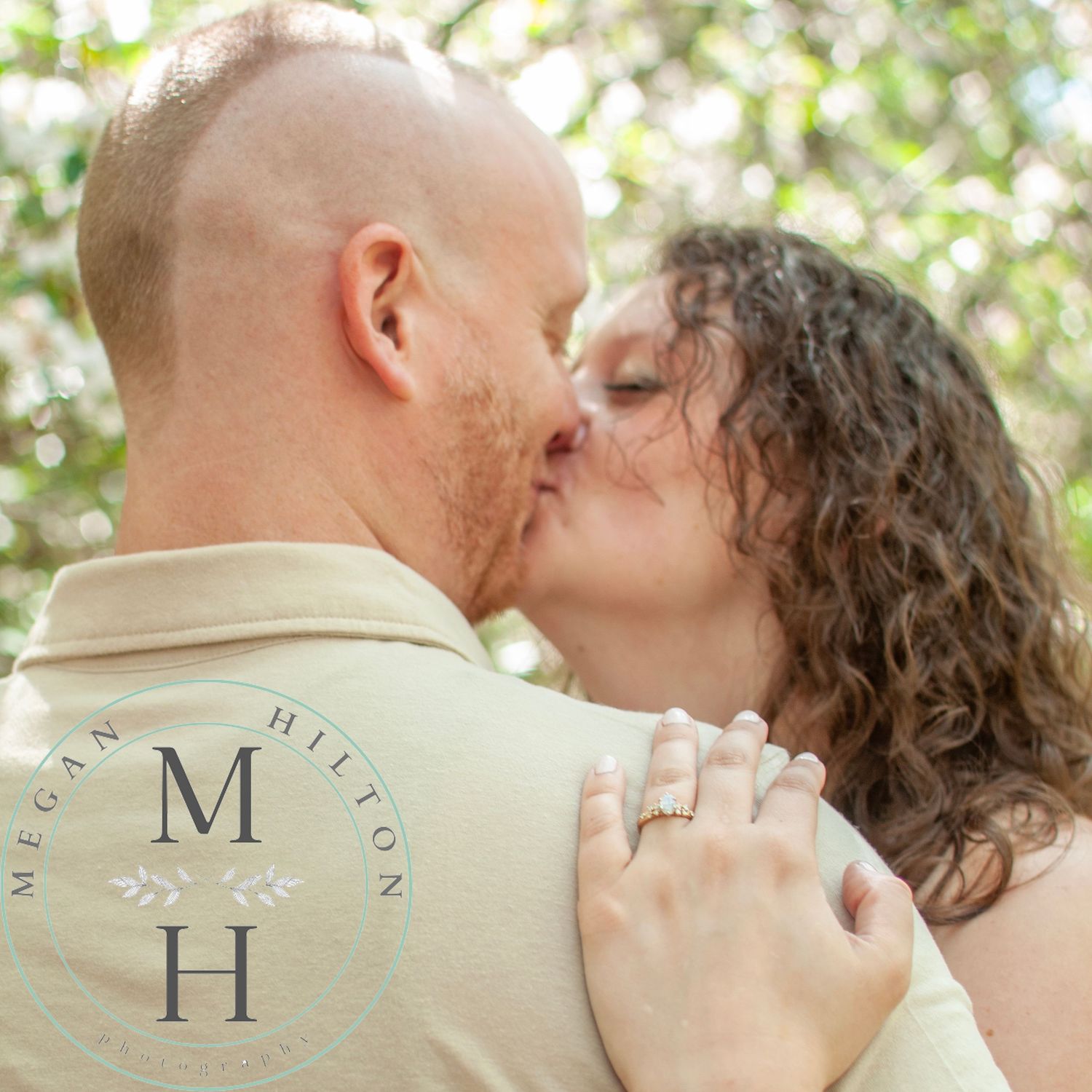 A couple shares a romantic kiss outdoors with natural bokeh lighting.