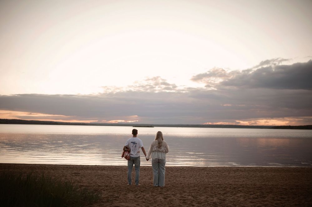 A couple stands silhouetted against a dramatic sunset sky on an empty beach.