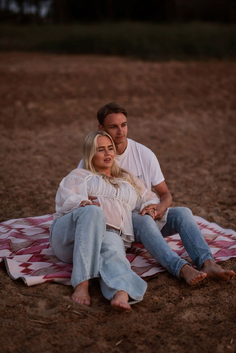 A romantic couple relaxes on a red checkered blanket in a field during golden hour.