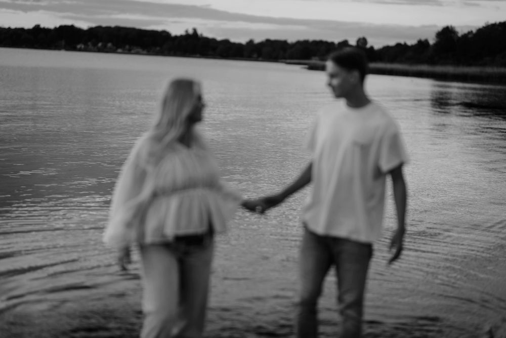 A blurry black and white image of a couple standing in shallow water at sunset by a lake.