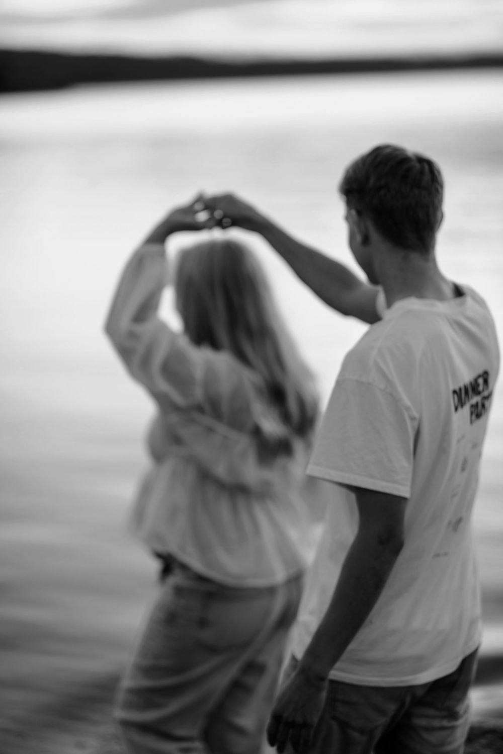 A soft black and white photo captures a couple walking together in matching white outfits.