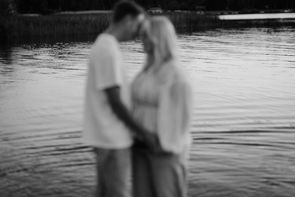 A romantic black and white photo of a couple embracing by a tranquil lake at sunset.