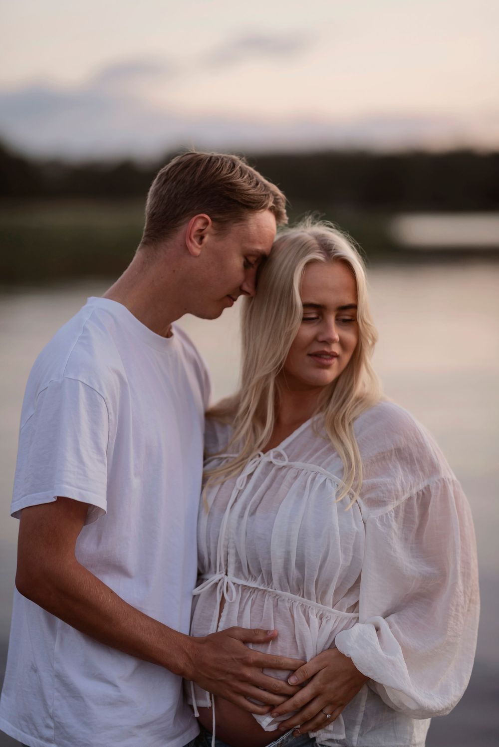 Tender interaction between couples wearing white outfits against a lakeside backdrop.
