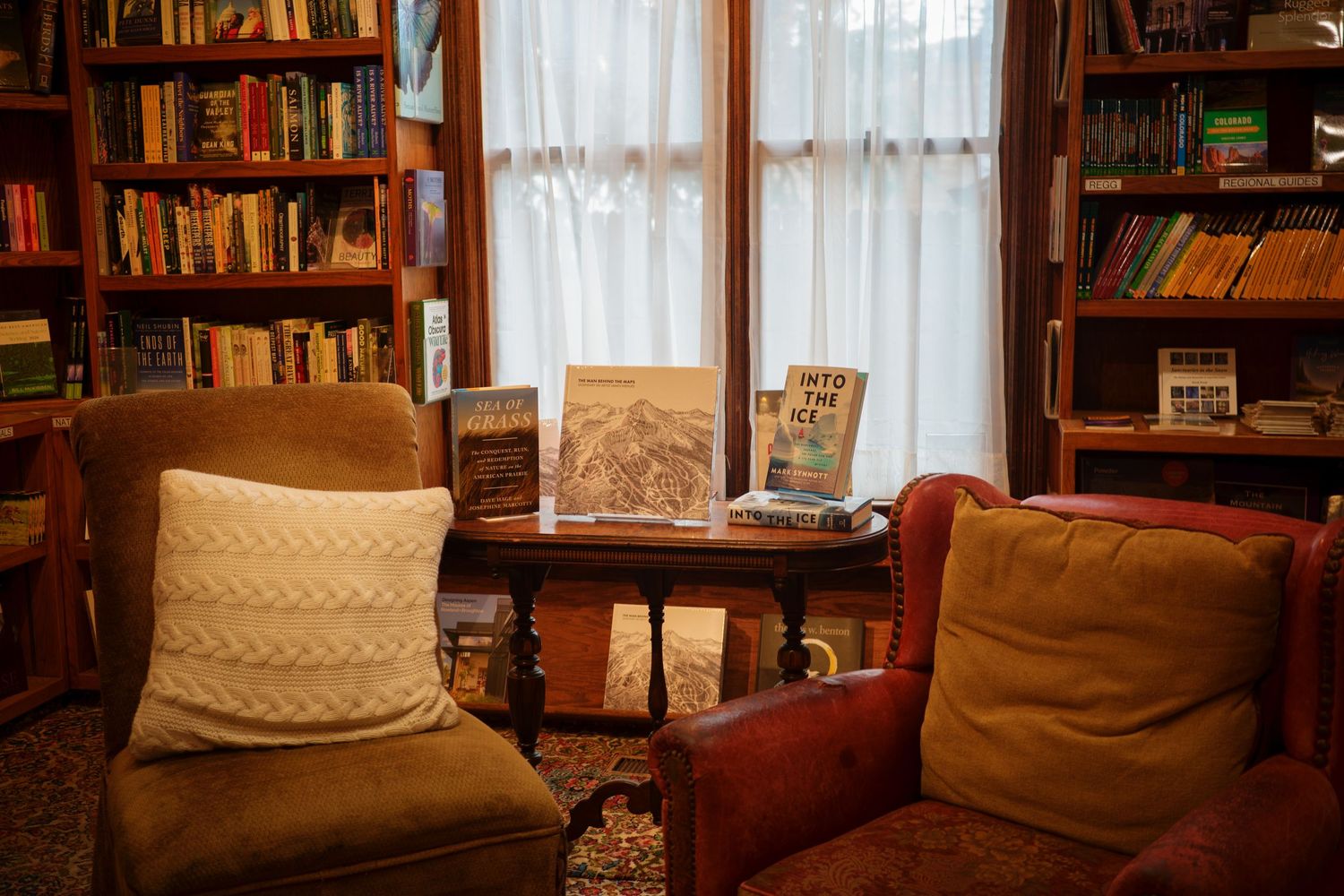 Cozy bookstore reading nook with two armchairs, cushions, and books on a small table.