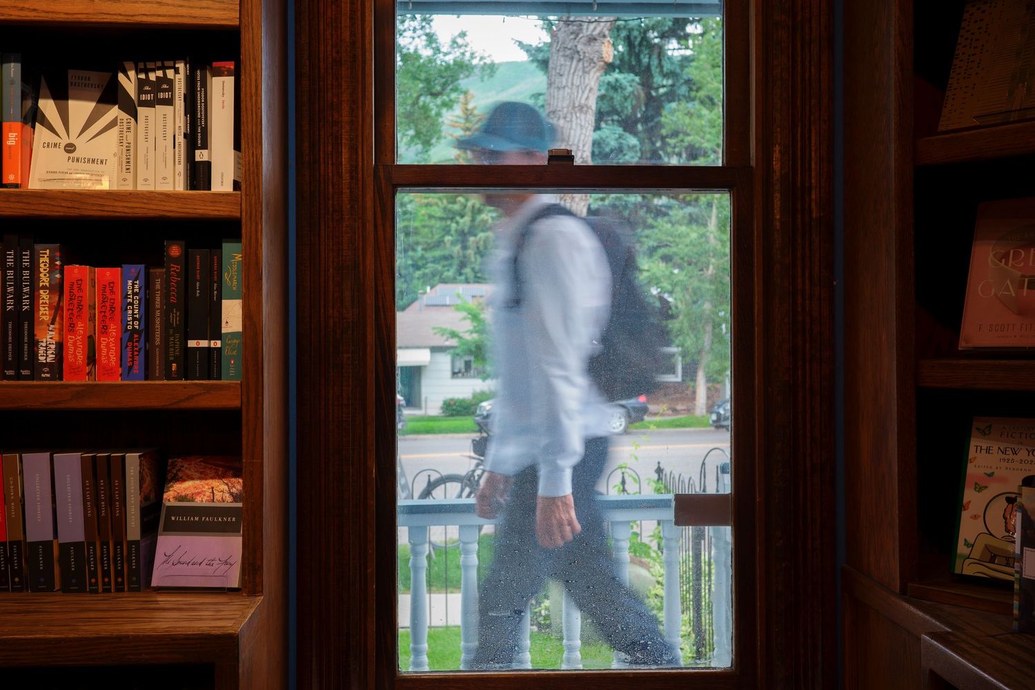 Blurred figure walking past a bookstore window with shelves of colorful books visible.