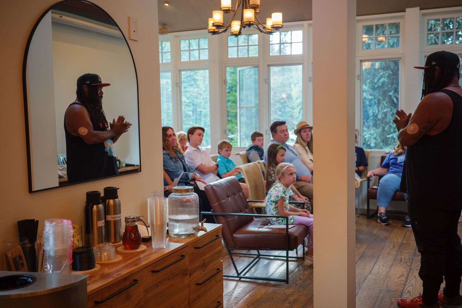 Speaker presenting to a seated audience in a bright, modern living room setting.