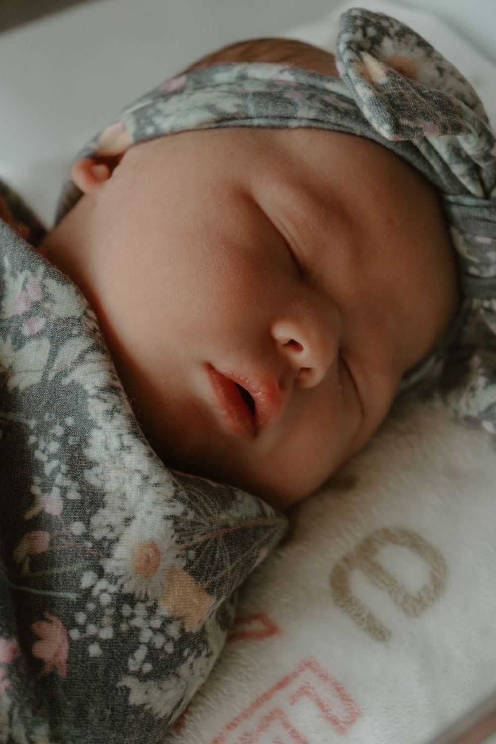 Close-up of a sleeping newborn baby wearing a floral headband and matching swaddle blanket.