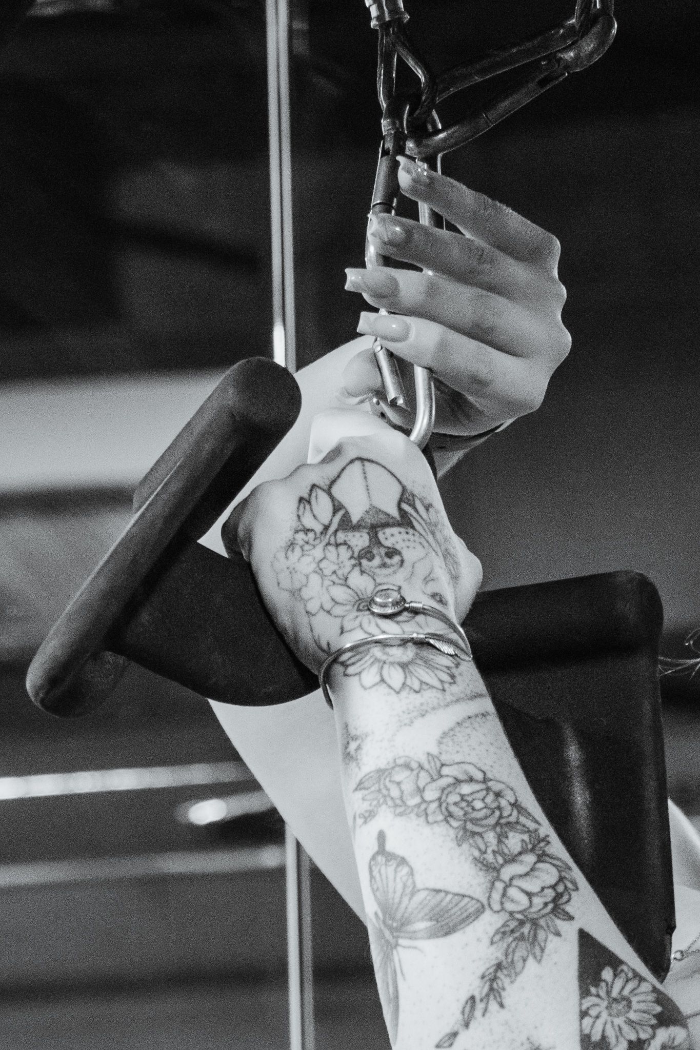 Close-up of tattooed arm and manicured hand gripping a cable machine handle, floral and butterfly ink in clear detail.