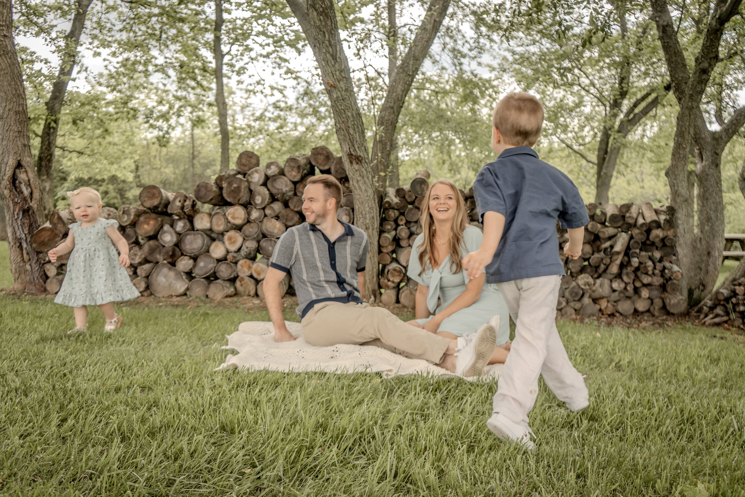 Family of four enjoying a relaxed outdoor picnic on a blanket surrounded by trees.