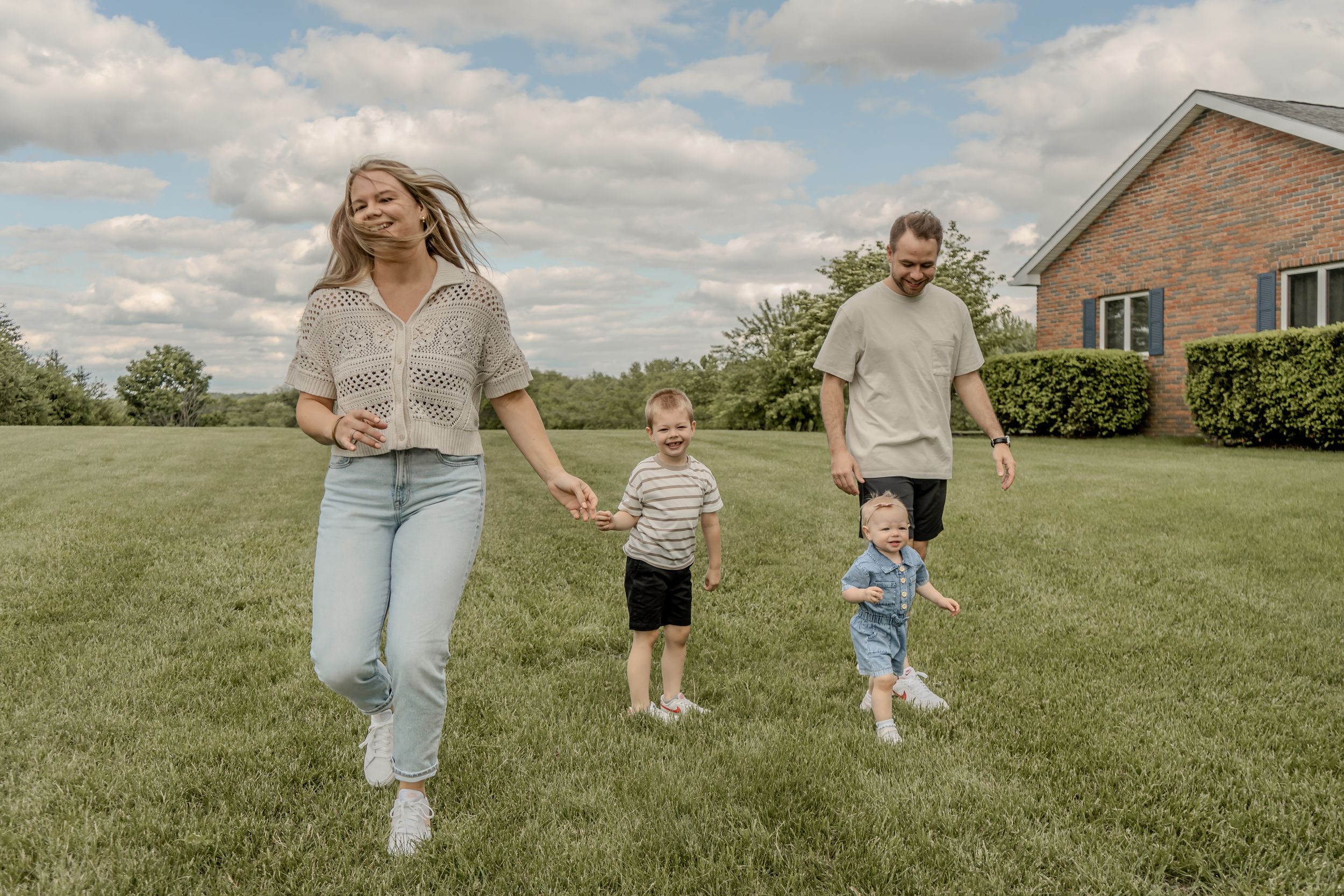 Joyful family running together on a green lawn outside a brick home on a sunny day.