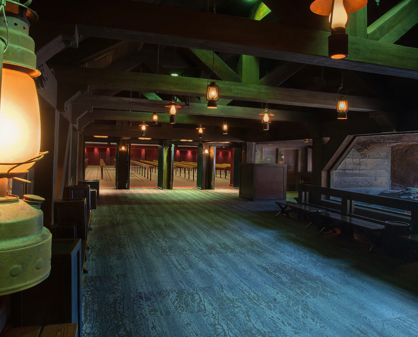 Dimly lit vintage ballroom with wooden floors and green columns illuminated by hanging lanterns.