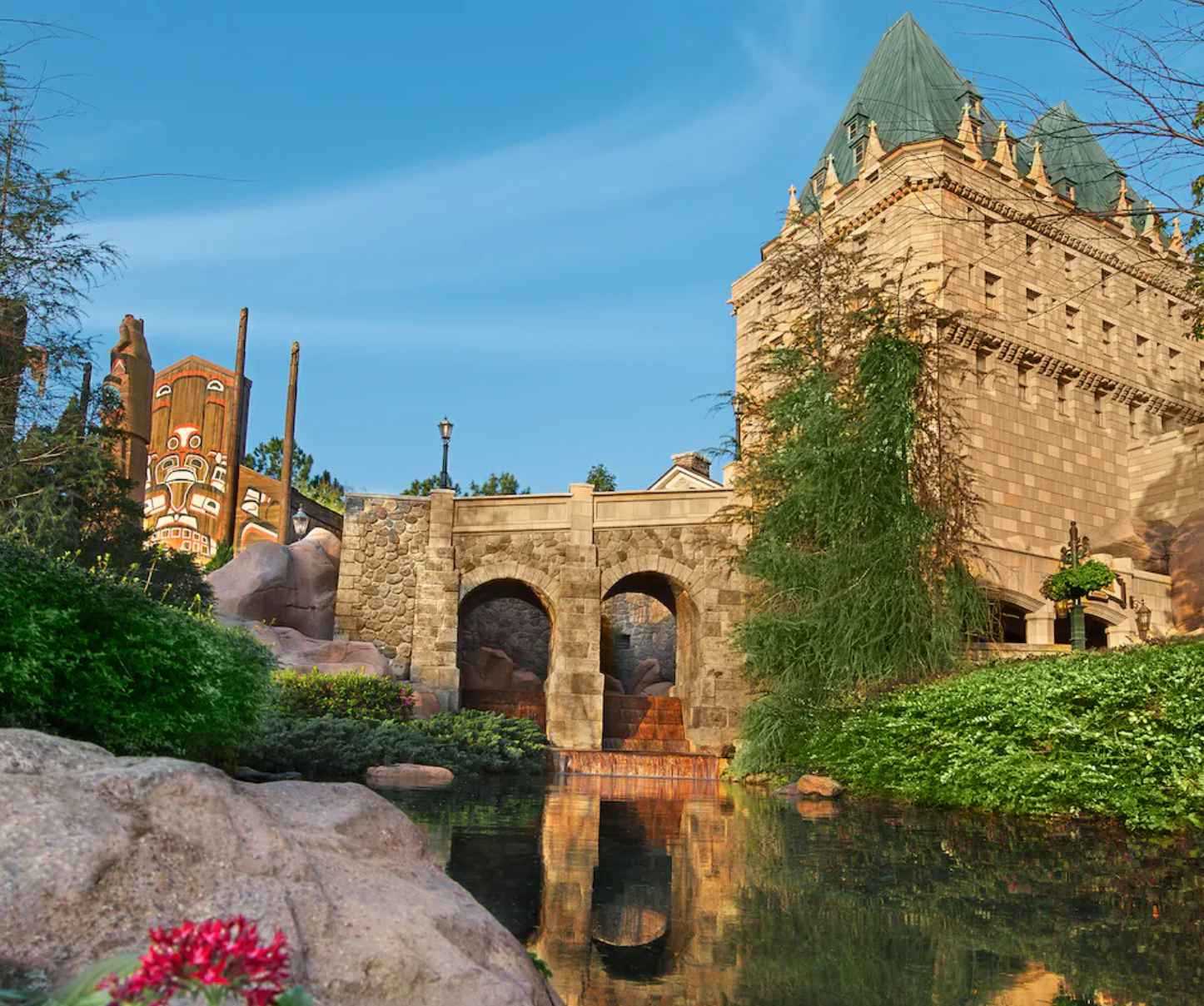 Medieval castle with stone bridge reflecting in pond surrounded by landscaped gardens.