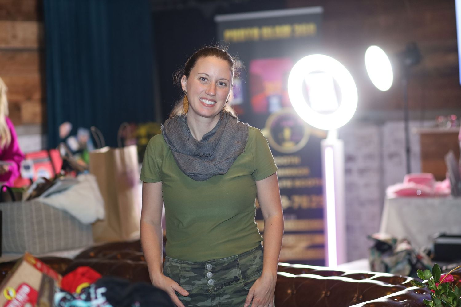 Someone wearing an olive green shirt and cowl neck scarf smiles in a retail setting with lighting fixtures visible in background.