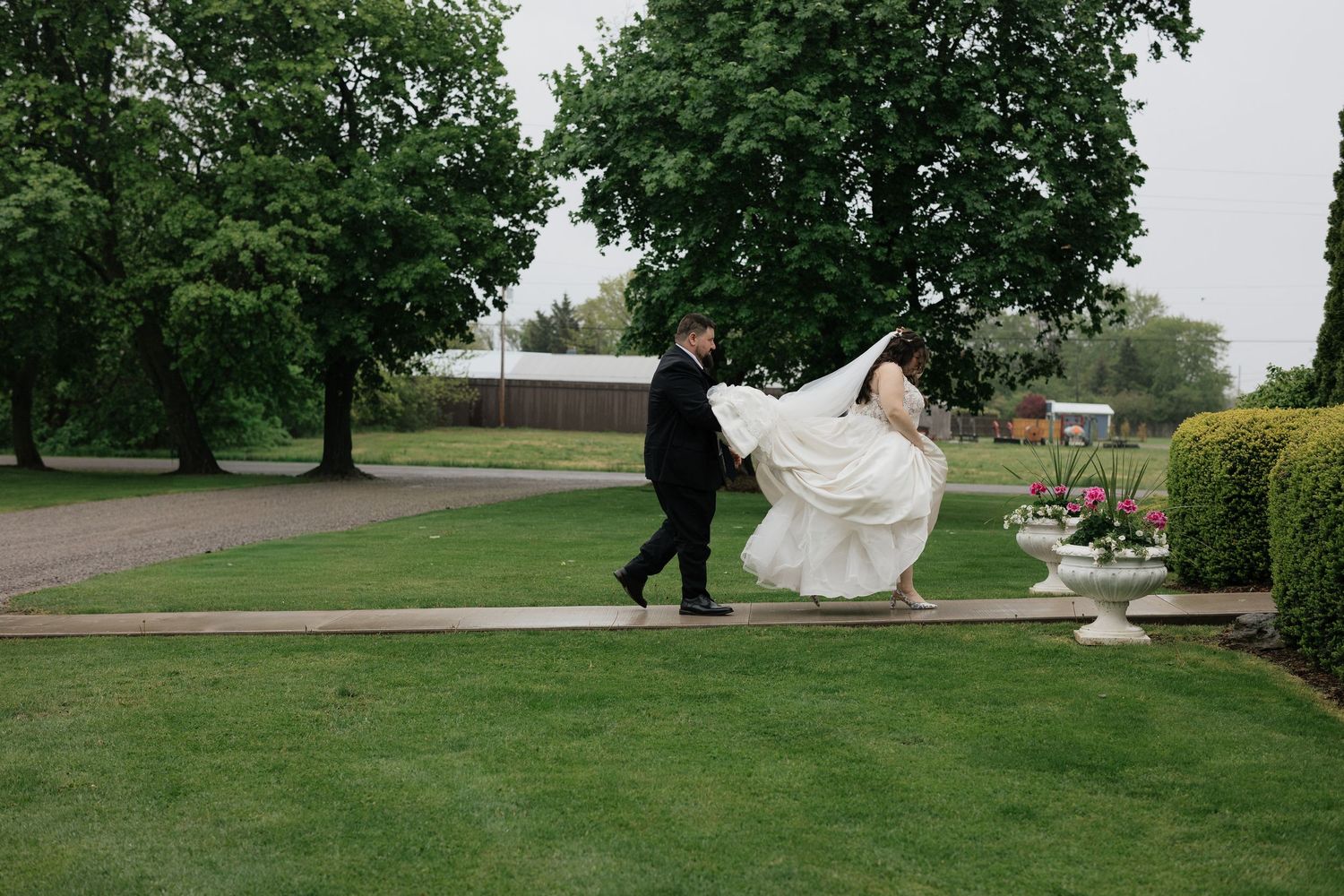 Two people share an intimate moment seated outdoors on a grey couch, with the person in white wearing a flowing veil.