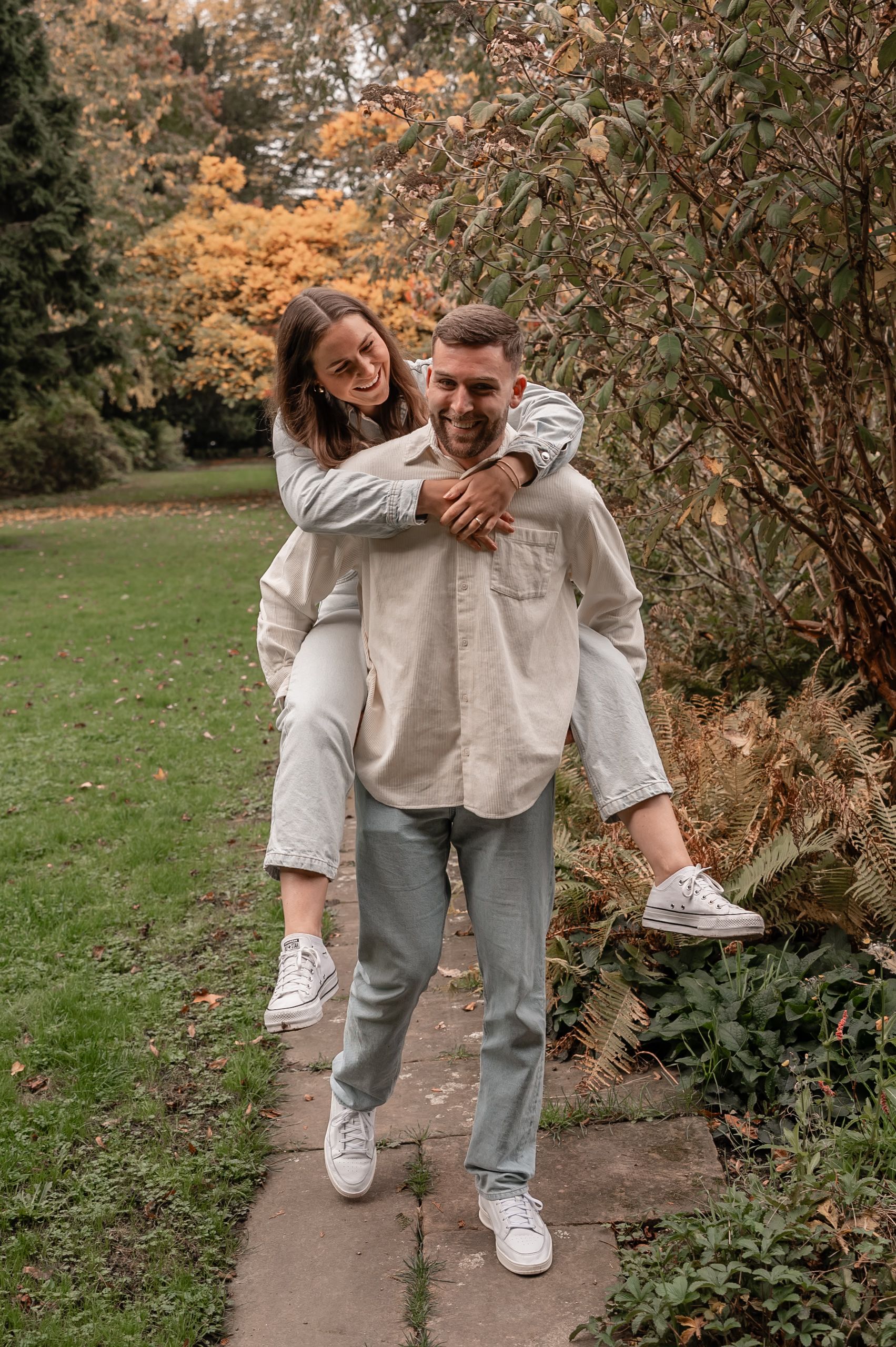 Couple in casual beige and gray outfits walking together on a garden path during autumn.