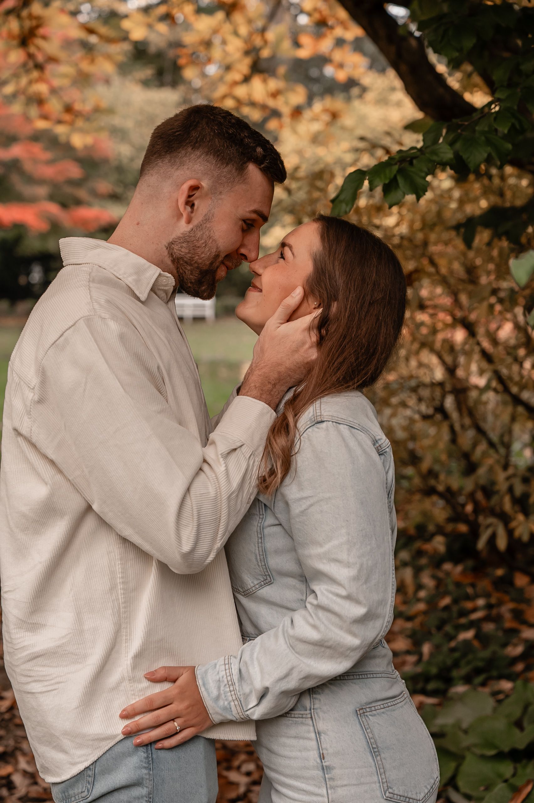 A romantic couple embraces under autumn trees with golden leaves during an outdoor photoshoot.