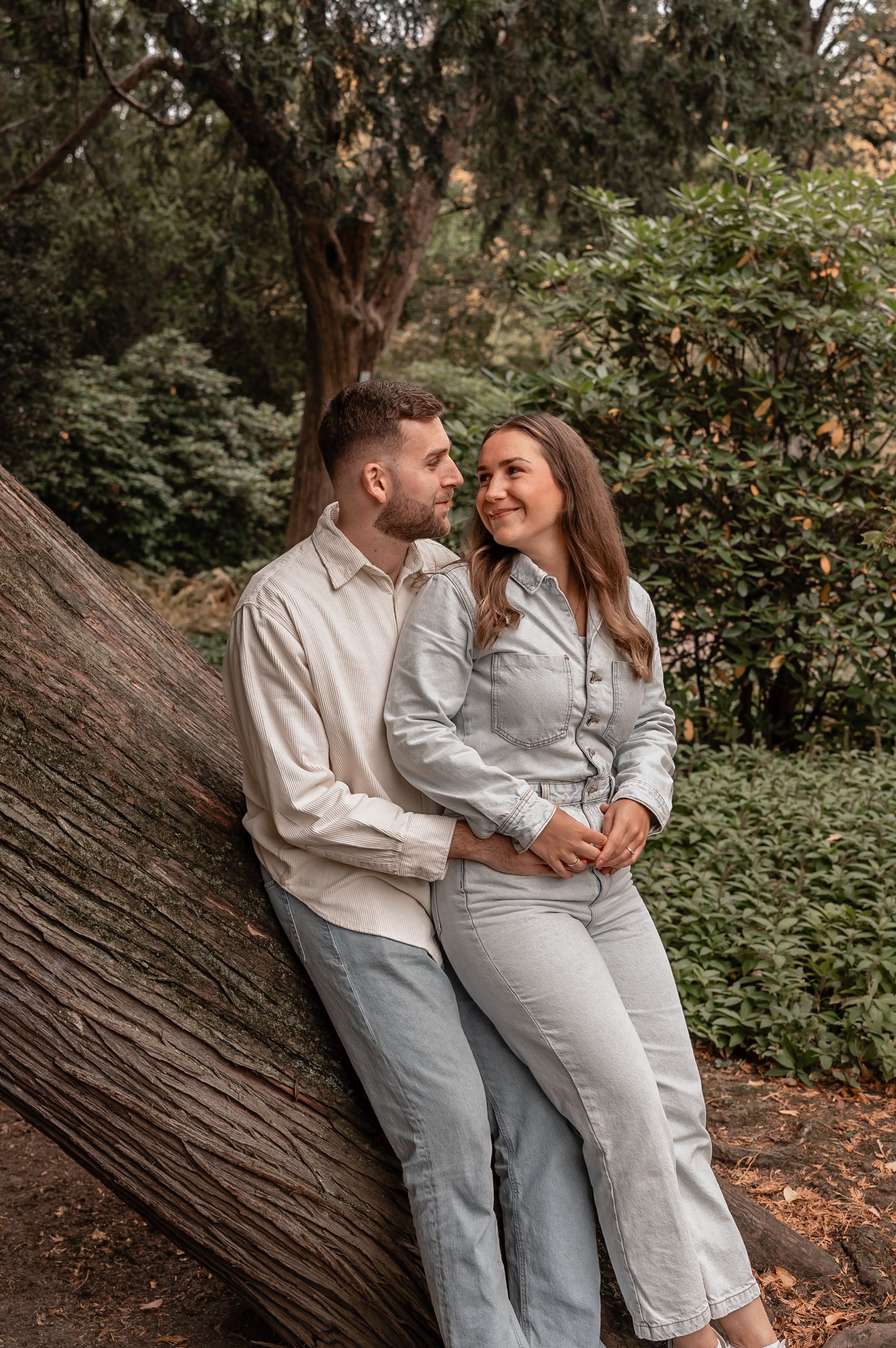A couple wearing matching white and gray outfits sits together on a fallen tree trunk in a wooded setting.