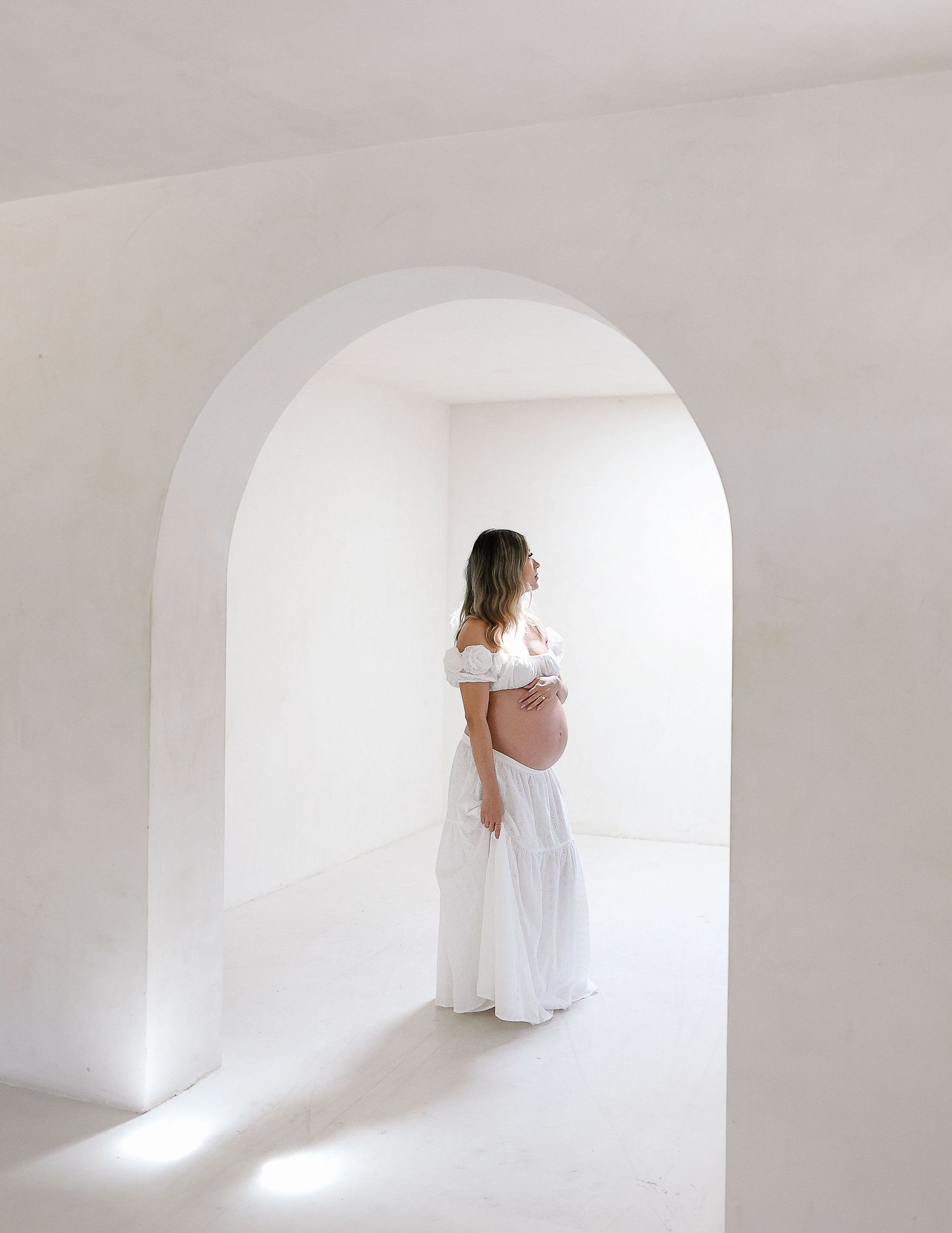 A series of four minimalist white archways with a figure in white flowing fabric creating an ethereal artistic effect.