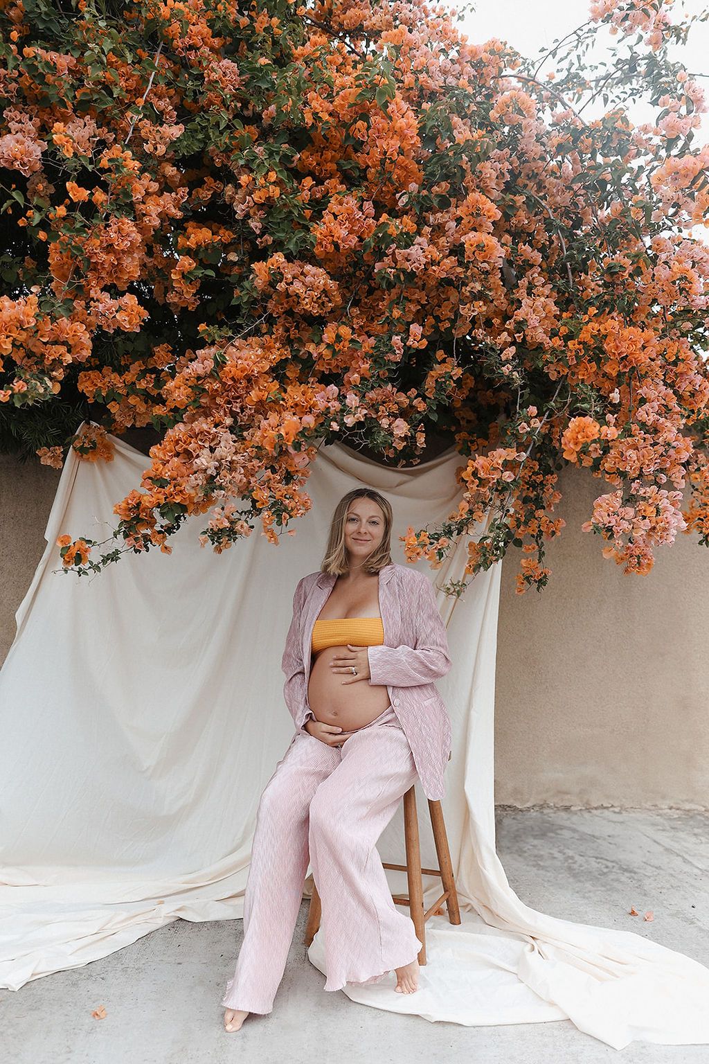 Maternity portrait with peach-colored flowers and white fabric backdrop.