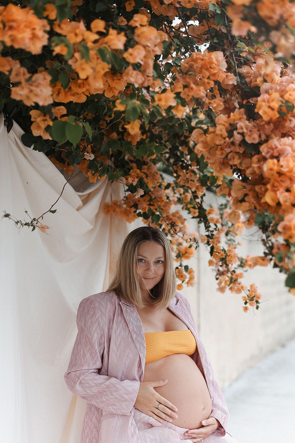 Beautiful maternity photo with coral orange bougainvillea flowers against white backdrop.