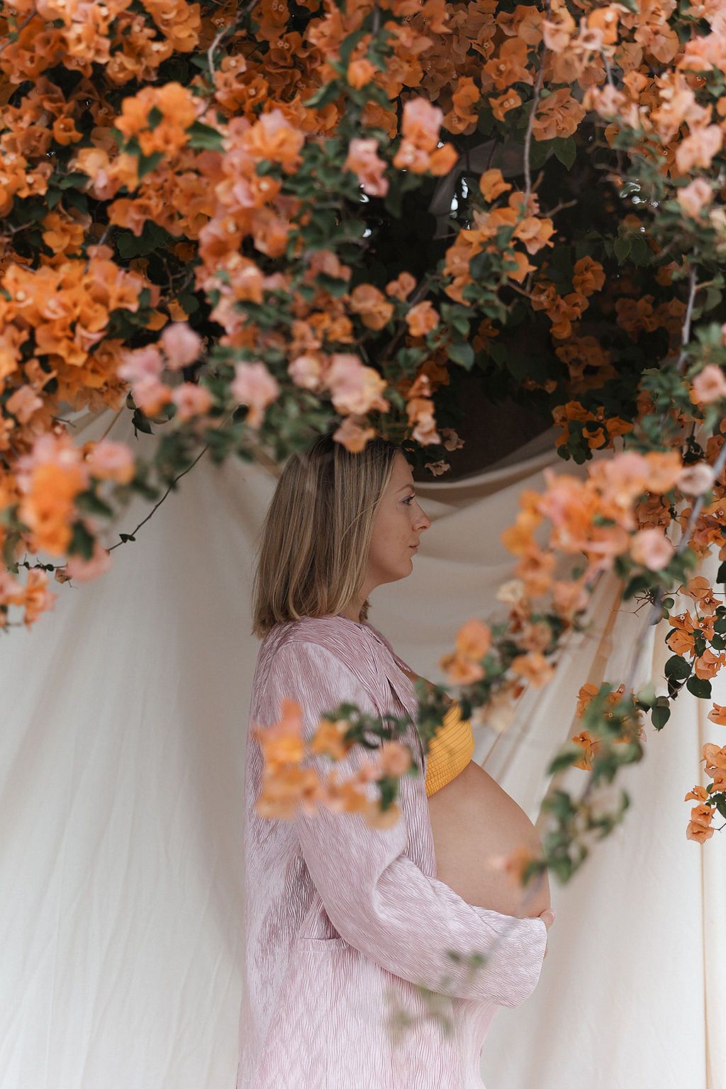 Side view maternity portrait framed by orange blossoms against white backdrop.