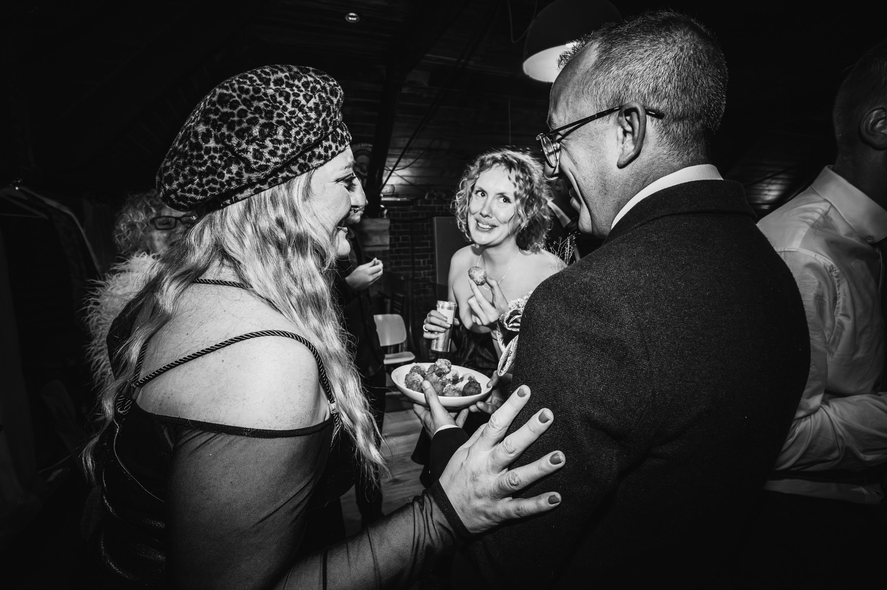 Black and white candid photo showing people engaged in animated conversation at what appears to be an evening social event.