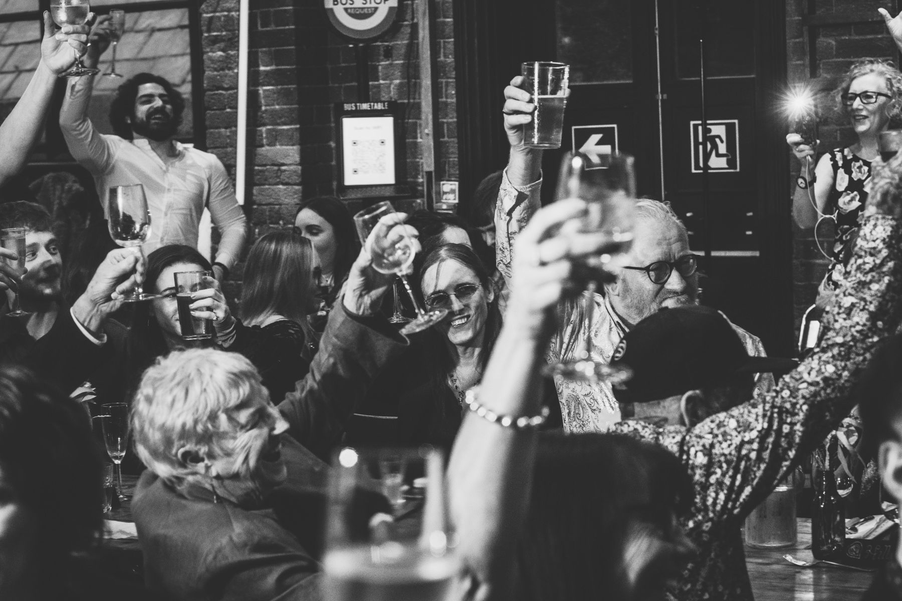Lively scene in a dim bar with patrons raising drinks and laughing together at a social gathering.