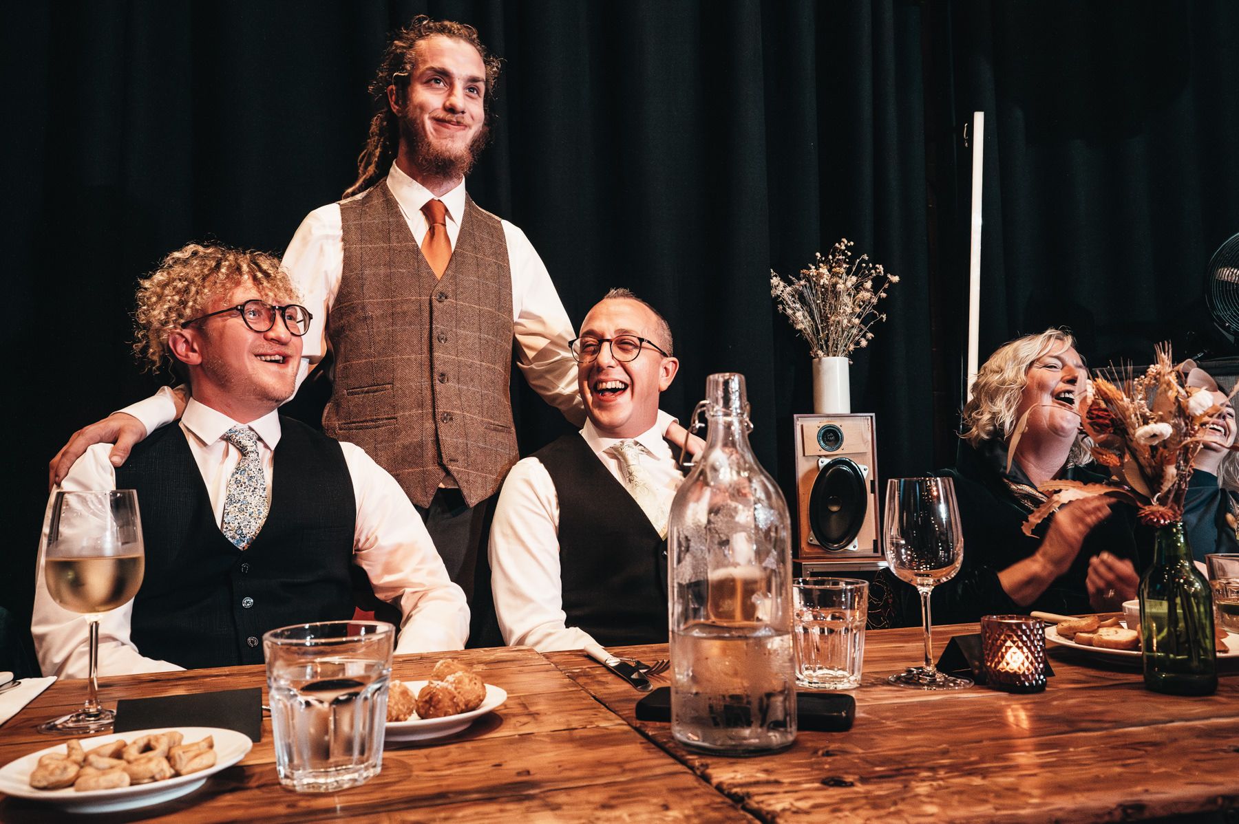 Group enjoying drinks and conversation at a rustic wooden bar counter with vintage-style lighting.
