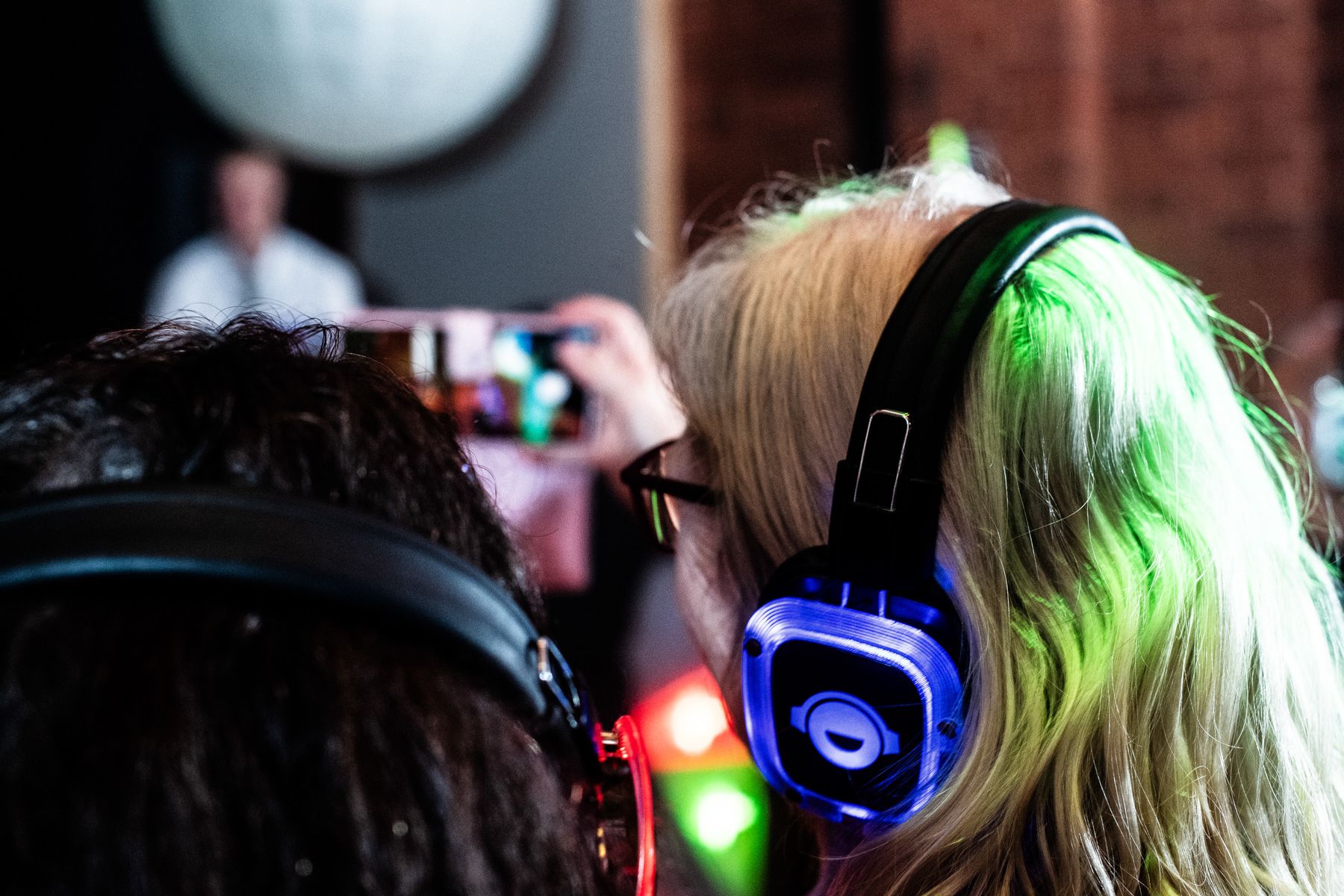 Silhouettes of party attendees wearing glowing headphones at a silent disco event.
