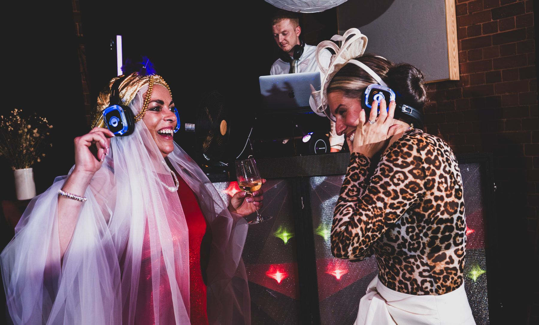 DJ wearing headphones and animal print performs at an energetic nightclub party with colorful lighting effects.
