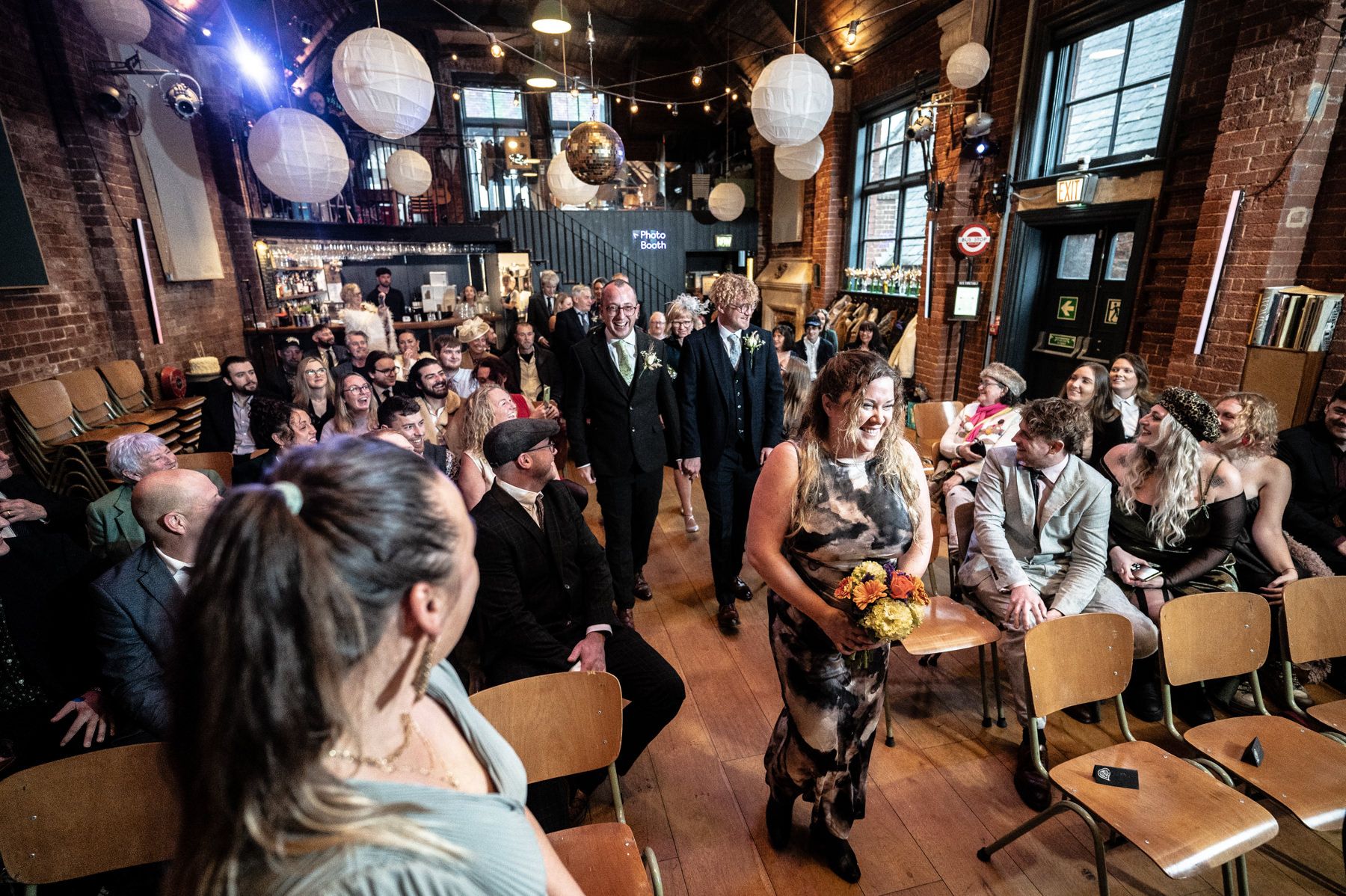 A dimly lit restaurant venue filled with guests seated in chairs while round paper lanterns hang from the ceiling.