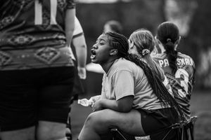 A group of young softball players sit together on a bench during a game, watching the action intently in black and white.
