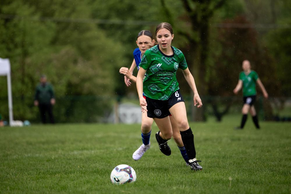 Soccer player in green jersey dribbles ball on grass field during competitive match.