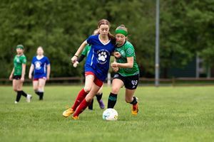 Two soccer players compete for control of the ball during an outdoor match on a grassy field.